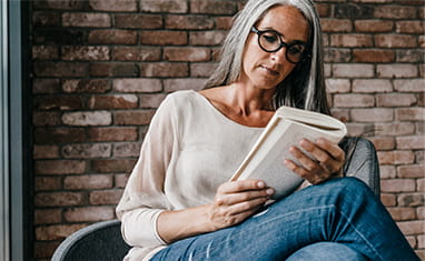 Woman with long grey hair sitting on chair reading book